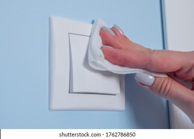 Disinfection, protection, prevention, housework, COVID 19, coronavirus, safety, sanitation concept. Woman hands cleaning white light switch on blue wall with antiseptic disinfectant wet wipe