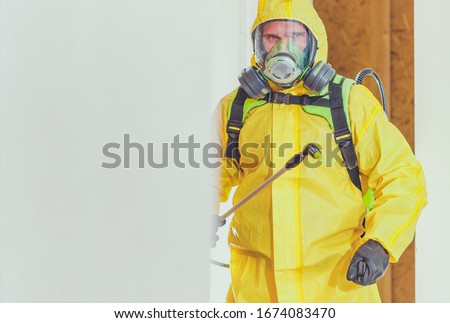Disinfection For Virus Killing. Worker in Hazmat Suit and Face Protection Mask Spraying  Interior Using Chemical Agents To Stop Spreading Virus Infections.