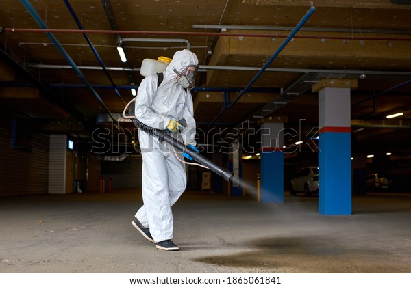 disinfector in\
medical suit working with pressure washer or sanitizer outdoors,\
wearing medical mask, gloves and\
goggles