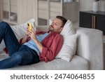 Disinterested man with phone lying on couch surfing online web, procrastination at home. Lazy male with social media addiction on smartphone scrolling internet, enjoy virtual life rest look at screen.