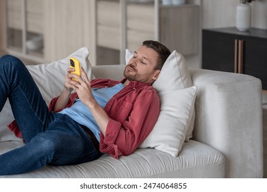 Disinterested man with phone lying on couch surfing online web, procrastination at home. Lazy male with social media addiction on smartphone scrolling internet, enjoy virtual life rest look at screen. - Powered by Shutterstock