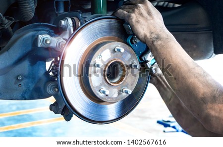 Disk brake and car disk brake system service concept - Car disk brake pad replacement service by hand of mechanic man in car garage with flare light effect and copy space