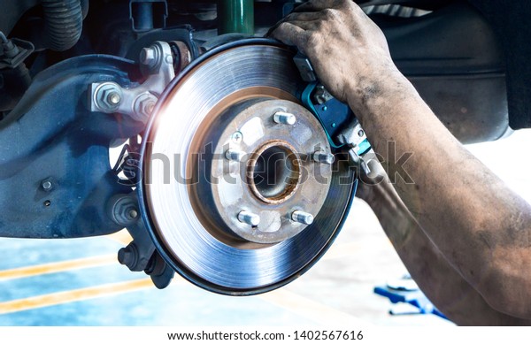 Disk brake and car disk\
brake system service concept - Car disk brake pad replacement\
service by hand of mechanic man in car garage with flare light\
effect and copy space