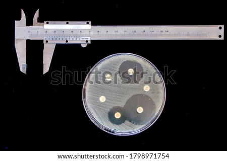 Disk Diffusion Susceptibility Test, measurement of the zone of inhibition of some antibiotics. Petri dish, callipers and vernier scale on black background. 