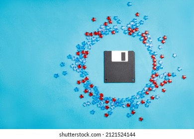 Diskette For A Computer Surrounded By Plastic Stars. Floppy Disk On Blue Fabric Background, Retro 90s Throwback