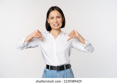 Dislike. Disgusted Asian Woman Showing Thumbs Down And Grimacing, Commenting On Smth Bad, Disagree, Complaining, Standing Over White Background