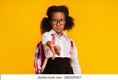 Dislike. Displeased Black Schoolgirl Gesturing Thumbs Down Judging And Disapproving Something Standing Over Yellow Background. Studio Shot