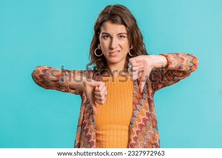 Dislike. Upset unhappy young woman showing thumbs down sign gesture, expressing discontent, disapproval, dissatisfied, dislike. Pretty attractive girl. Indoors isolated on blue studio background