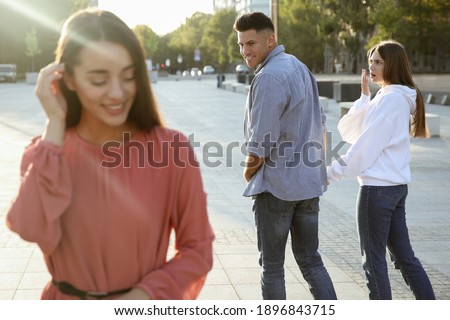 Disloyal man looking at another woman while walking with his girlfriend outdoors