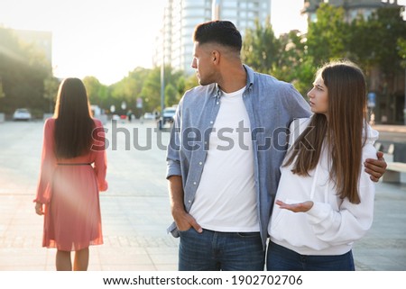Disloyal man looking at another woman while walking with his girlfriend outdoors
