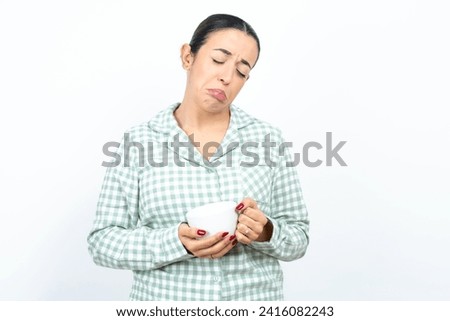 Dismal gloomy rejected Beautiful young woman wearing green plaid pyjama and holding a cup has problems and difficulties, curves lower lip and closes eyes in despair, being in depression