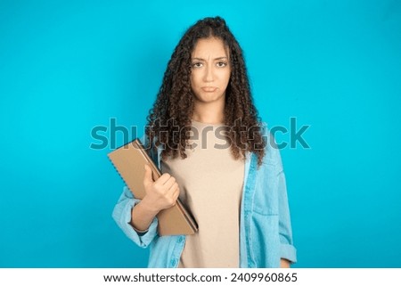 Dismal gloomy rejected Student arab girl with curly hair holding books has problems and difficulties, curves lower lip and closes eyes in despair, being in depression