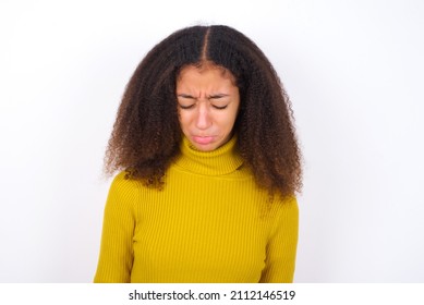 Dismal Gloomy Rejected Young Teen Girl Wearing Yellow Knitted Sweater Against White Background Has Problems And Difficulties, Curves Lower Lip And Closes Eyes In Despair, Being In Depression