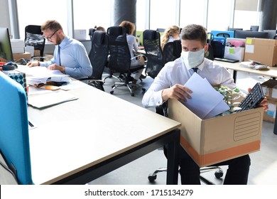 Dismissal Employee In Preventive Medical Mask In An Epidemic Coronavirus. Sad Dismissed Worker Are Taking His Office Supplies With Him From Office.