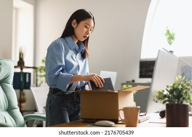 Dismissal. Frustrated Fired Asian Employee Woman Packing Belongings In Cardboard Box Leaving Workplace Standing In Modern Office Indoor. Staff Reduction, Unemployment Problem Concept