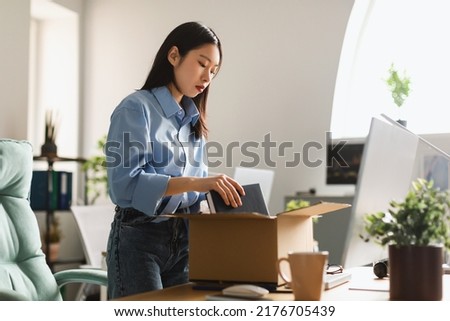 Dismissal. Frustrated Fired Asian Employee Woman Packing Belongings In Cardboard Box Leaving Workplace Standing In Modern Office Indoor. Staff Reduction, Unemployment Problem Concept Foto d'archivio © 