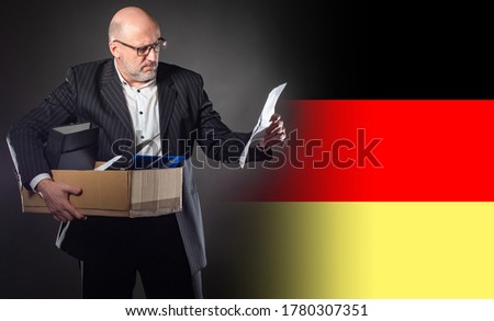 Dismissed man of Germany. Dismissed man holds a box. Unemployed next to flag of Germany. Dismissed man in a business suit. Concept - mass cuts in Germany. German reads a letter of resignation
