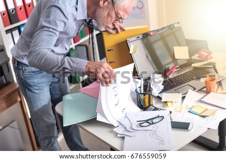 Disorganized businessman looking for documents on his desk, light effect