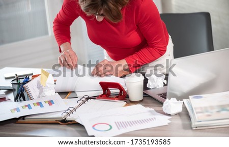 Disorganized businesswoman looking for documents on her messy desk