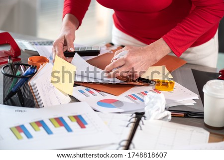 Disorganized businesswoman looking for documents on her messy desk