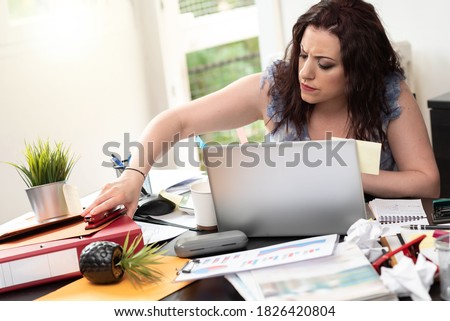 Disorganized young businesswoman looking for documents on her messy desk