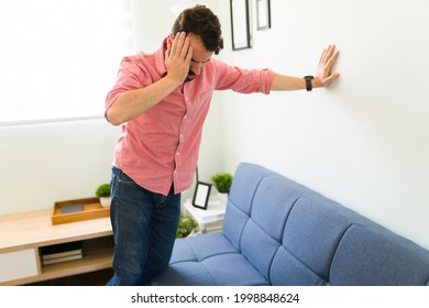 Disoriented man in his 30s feeling dizzy and trying to balance against a wall background. Sick man with vertigo illness