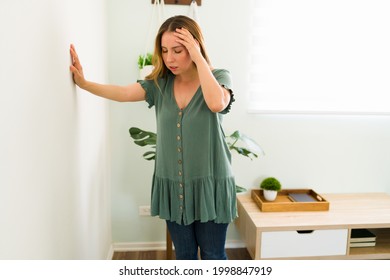 Disoriented Woman In Her 20s Feeling Dizzy And Trying To Balance Against A Wall Background. Sick Woman With Vertigo Illness