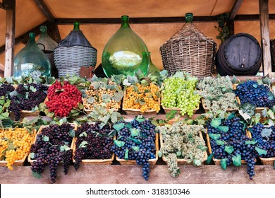 Display of assorted colored grapes in wicker trays below a shelf of old wine storage bottles in a winery, tavern or market, conceptual of viticulture, agriculture and wine making