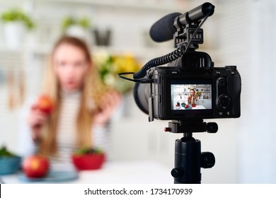 Display of camera recording video blog for food blogger woman with apple, pineapple in kitchen studio talking about healthy vegan eating. Influencer vlogger girl live streaming nutrition masterclass.