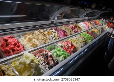 A display case with various types of ice cream for sale and customers on the streets of Budva in the evening. Montenegro