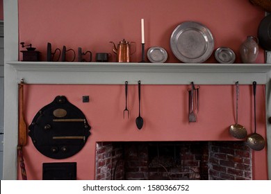 A Display In A Colonial Home Kitchen. An Assortment Of Utensils, Candles, A Fireplace, Dishes, And Giant Spoons.