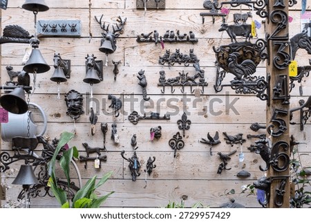 Display of decorative cast iron objects on a rustic wooden wall. Collection of vintage style hooks, bells, and animal figures including cats, birds, and deer for garden or home decor