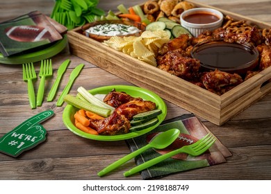 Display of football tailgate party foods in a wooden box filled with chicken wings, wieners, chips, pretzels, vegetables, dips and sauces surrounded by football themed decorations