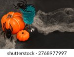A display shows two pumpkins, one large and one small, near a blue drink served in a skull glass. Fake spiders are scattered around and a web like material is present.