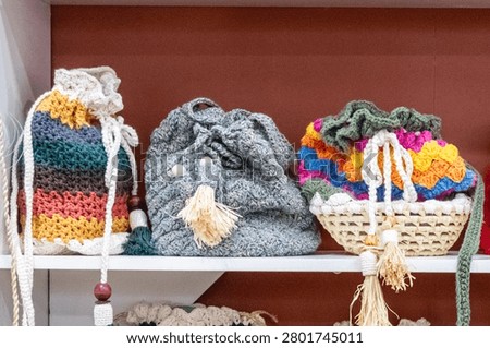 Display of three handmade crochet drawstring bags with straw and wooden details on a white shelf. Sharp technical focus and terracotta background.