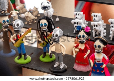 A display of various dolls and figures, including some with skulls on their faces. The dolls are arranged on a shelf. Day of the Dead celebration in Mexico, papel picado crafts, offerings, La Catrina