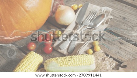Displaying pair of corn cobs resting on rustic kitchen tabletop, with pumpkin and tied silverware. Maize, tomatoes, stilllife, warmlight, autumn, harvest, burlap