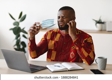 Displeased African Man Taking Off Mask At Work To Scratch Beard, Suffering From Itchy Face Skin, Stressed Black Male In Traditional Clothes Having Allergy, Sitting At Workplace In Office, Free Space