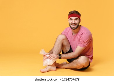 Displeased Bearded Fitness Sporty Guy Sportsman In Headband T-shirt In Home Gym Isolated On Yellow Background. Workout Sport Motivation Concept. Get Injured Hold Ice Pack Cooling Down Ankle Foot Pain