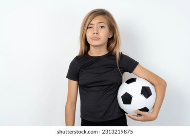 Displeased beautiful caucasian teen girl wearing sportswear holding a football ball over white wall frowns face feels unhappy has some problems. Negative emotions and feelings concept - Powered by Shutterstock