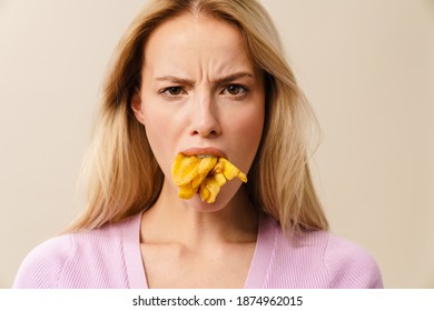Displeased beautiful girl posing with french fries in her mouth isolated over white background