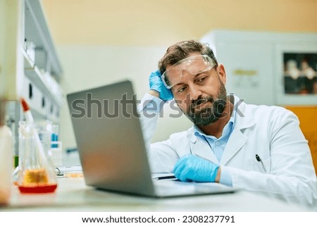 Displeased biochemist thinking of solution while working on laptop in laboratory.