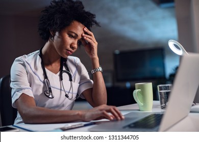 Displeased black healthcare worker using computer and reading an e-mail at doctor's office. 