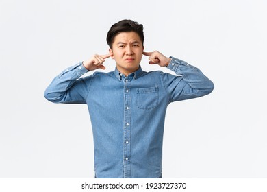 Displeased And Bothered Asian Male Student Complaining Loud Neighbour, Grimacing Displeased, Shut Ears With Fingers And Looking Annoyed, Disturbed With Loud Sound, Standing White Background