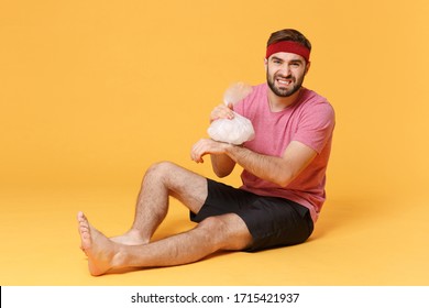 Displeased Fitness Sporty Guy 20s Sportsman In Headband T-shirt In Home Gym Isolated On Yellow Background. Workout Sport Motivation Concept. Get Injured Hold Ice Pack Cooling Down Hand Wrist Pain