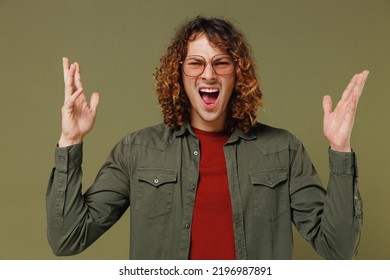 Displeased Irritated Frustrated Sad Upset Long Curly Hair Young Brunet Man 20s Wears Khaki Shirt Jacket Glasses Raise Hands Palms Up Shout Yell Isolated On Plain Olive Green Background Studio Portrait