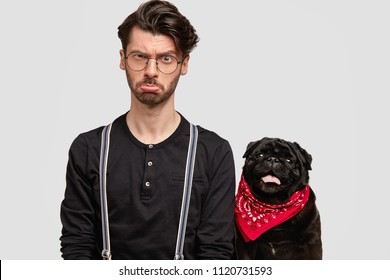 Displeased Male Dog Trainer Purses Lips And Has Unhappy Expression, Trendy Haircut, Poses Near Pet, Isolated Over White Bsckground. Stylish Hipster Going To Have Walk Outside, Being In Bad Mood