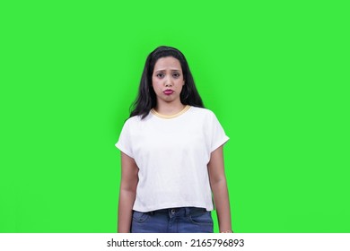 Displeased Or Sad Woman Making Cute Facial Expression Like A Child, Standing Straight Looking At Camera, Isolated Over Green Background. Sad, Unhappy, Displeased, Hurt, Emotional Expressions.