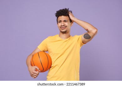 Displeased Sad Young Fan Man Of African American Ethnicity Wear Casual Yellow T-shirt Posing Play Basketball Hold Ball Put Hand On Head Isolated On Plain Pastel Light Purple Background Studio Portrait