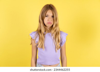 Displeased upset Caucasian kid girl wearing violet T-shirt over yellow background frowns face as going to cry, being discontent and unhappy as can't achieve goals,  Disappointed model has troubles - Shutterstock ID 2344462255